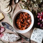 Christmas Ale Chutney on a cheeseboard surrounded by salami, cheeses, grapes and crackers.