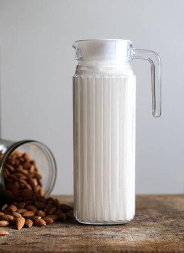 A jug of Homemade Almond Milk next to some almonds