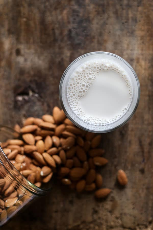 overview of a jug of Homemade Almond Milk next to some almonds