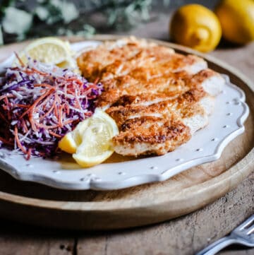 side view of Plate of Gluten-Free Chicken Schnitzel with coleslaw and lemon