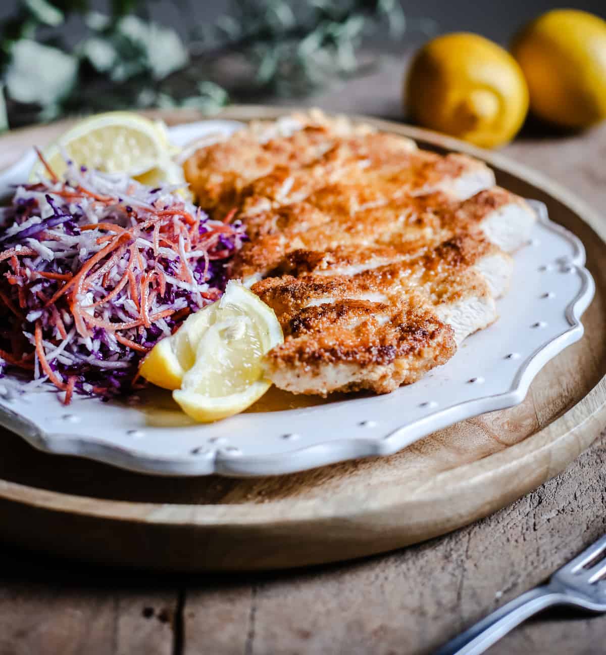 side view of Plate of Gluten-Free Chicken Schnitzel with coleslaw and lemon