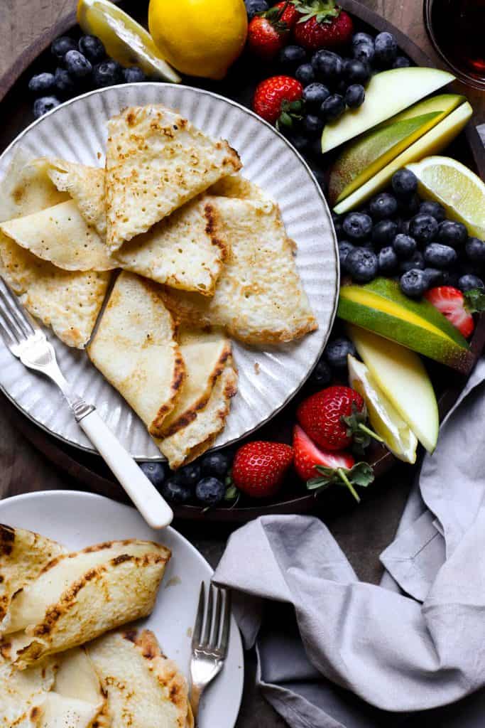 A plate of pancakes with ice cream, maple syrup and a fruit platter