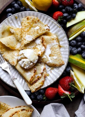 A plate of pancakes with ice cream, maple syrup and a fruit platter