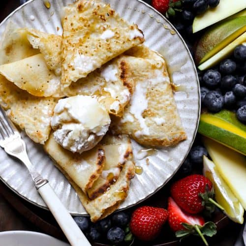 A plate of pancakes with ice cream, maple syrup and a fruit platter