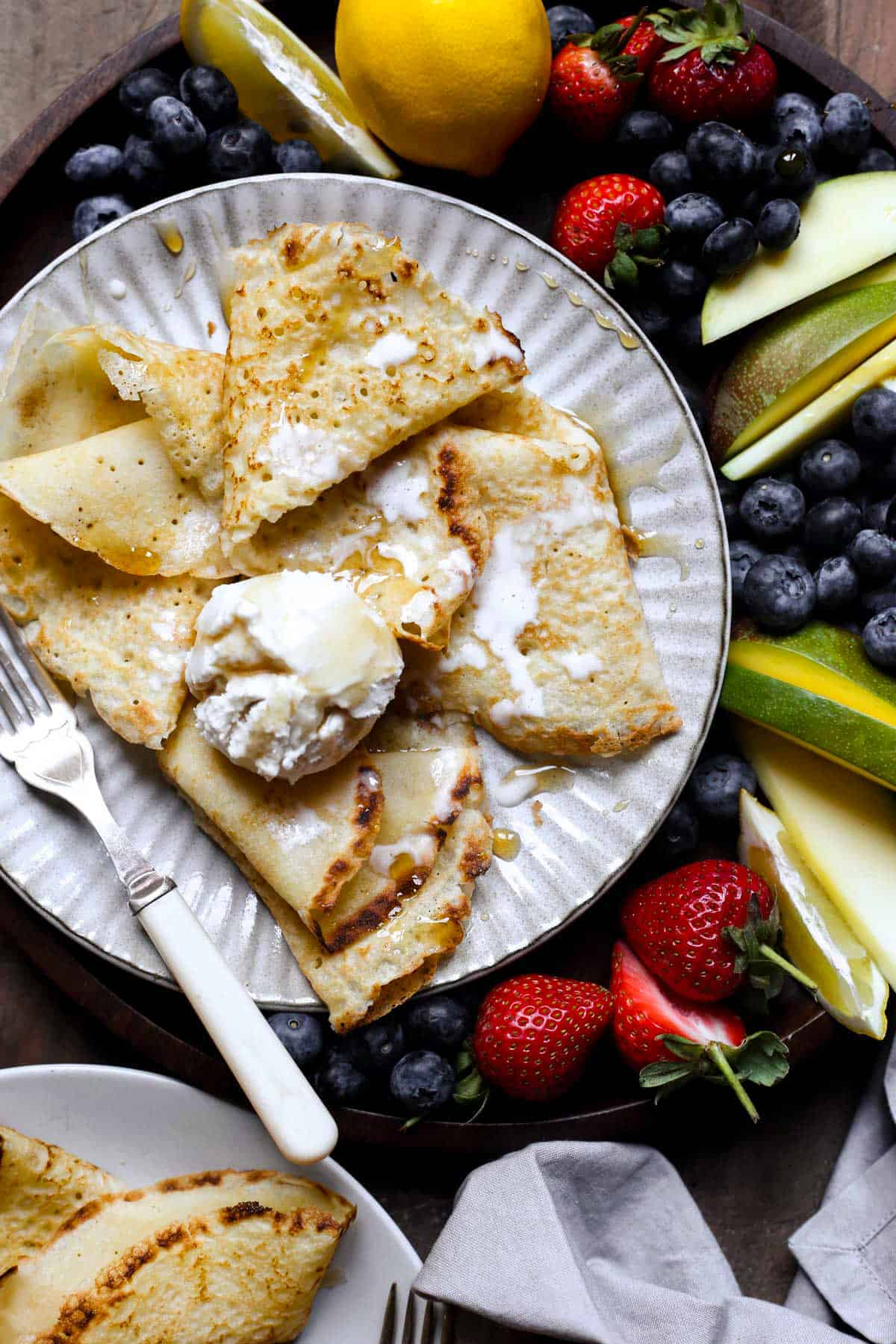 A plate of pancakes with ice cream, maple syrup and a fruit platter