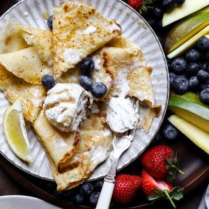 A plate of pancakes with ice cream, maple syrup and a fruit platter