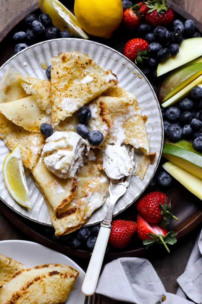 A plate of pancakes with ice cream, maple syrup and a fruit platter