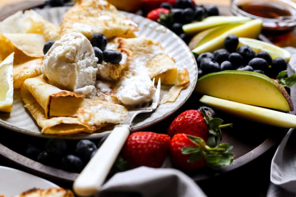 A plate of pancakes with ice cream, maple syrup and a fruit platter