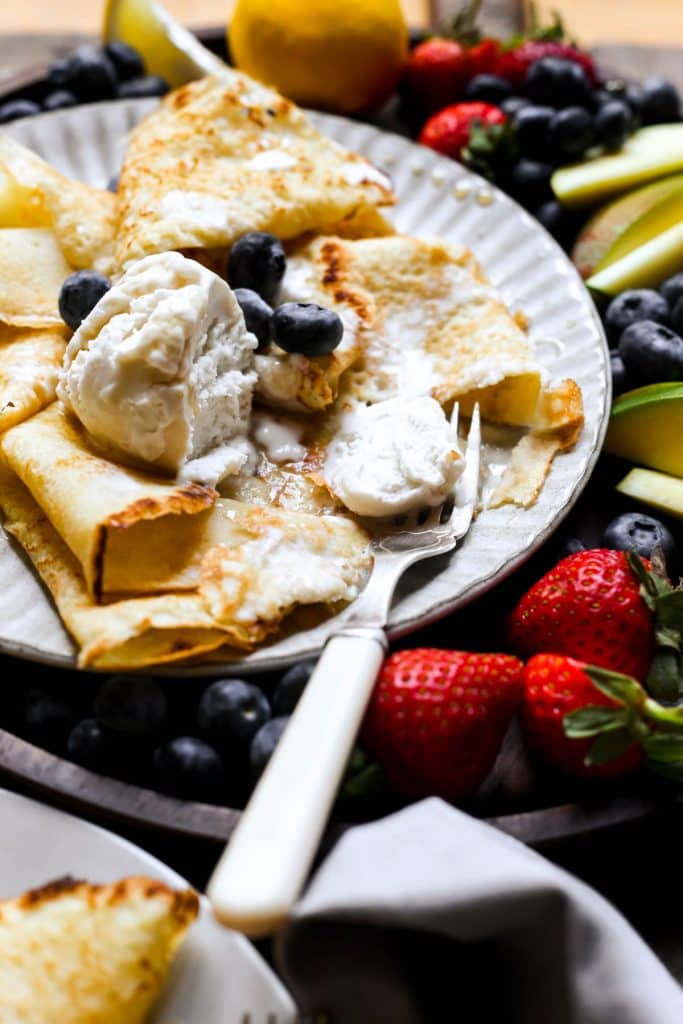 A plate of pancakes with ice cream, maple syrup and a fruit platter