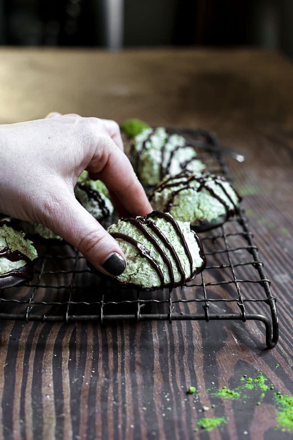 Coconut Matcha Macaroons on a wire rack with a hand picking one up