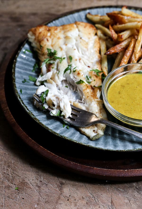 A plate of fish and chips with curry sauce with a bite taken out