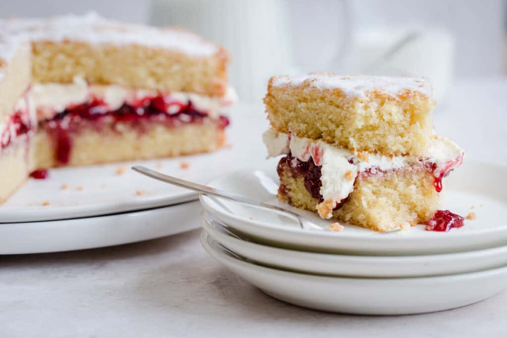 slice of victoria sponge with bite taken out on plate next to whole cake