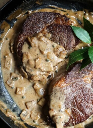 Two steaks in a pan with dairy-free peppercorn sauce