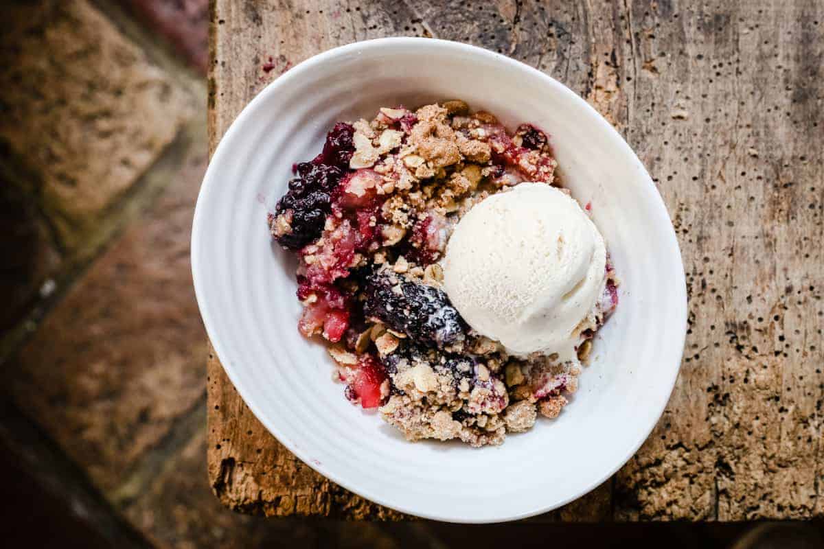 A bowl of apple and blackberry crumble with ice cream on top