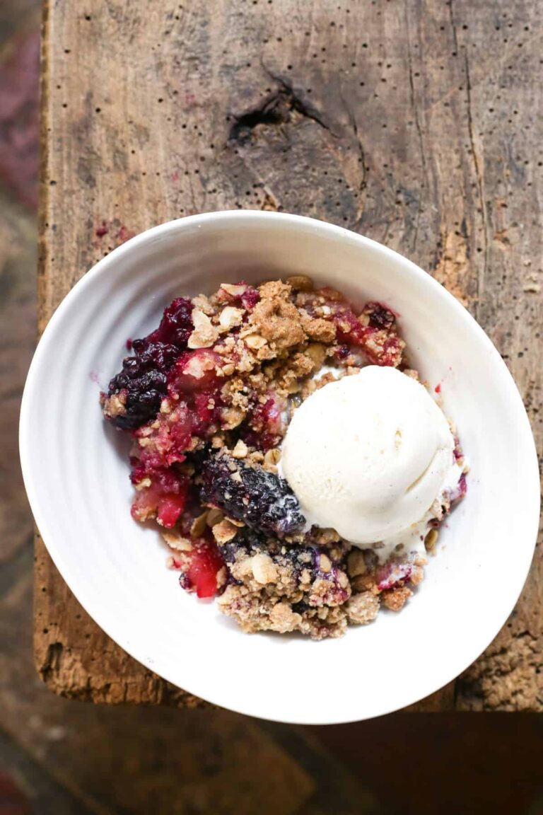 A bowl of apple and blackberry crumble with a scoop of vanilla ice cream in a bowl