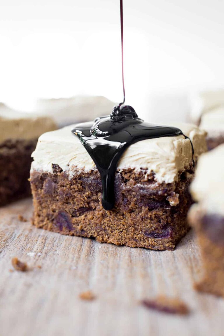 A slice of Sticky Date Cake on a wooden board with a drizzle of black treacle.