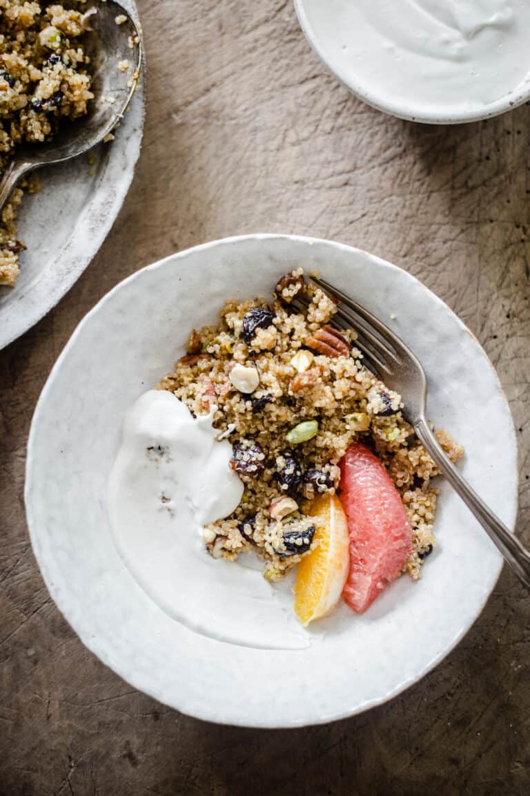 A bowl of Breakfast Quinoa with cashew cream and citrus fruits on a wooden board