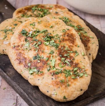 Pile of freshly made Naan on wooden board sprinkled with coriander.