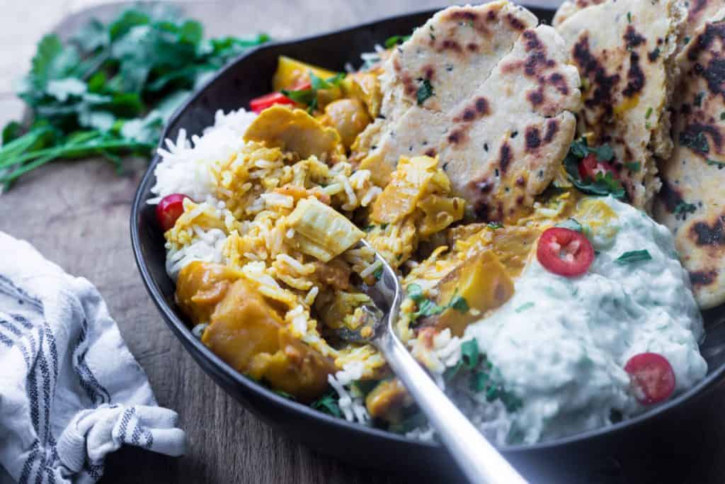 A bowl of The Best Totally Creamy Leftover Turkey Curry with naan bread, raita and rice