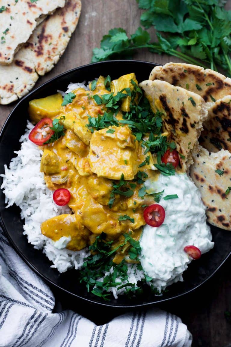 A bowl of The Best Totally Creamy Leftover Turkey Curry with naan bread, raita and rice