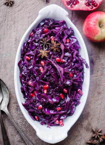 Braised Red Cabbage sprinkled with pomegranate seeds and star anise in a white dish on a wooden board