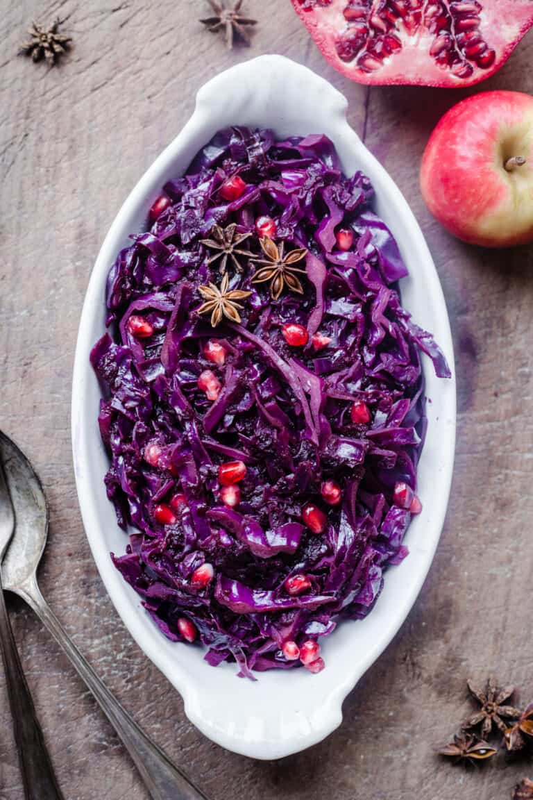 Braised Red Cabbage sprinkled with pomegranate seeds and star anise in a white dish on a wooden board