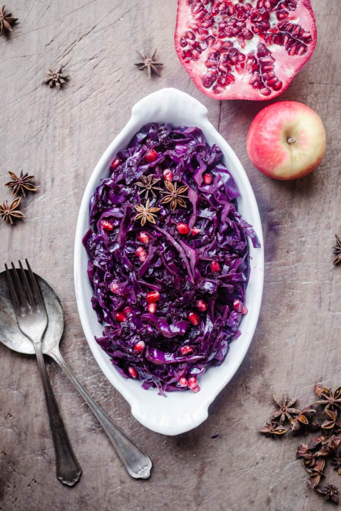 Braised Red Cabbage sprinkled with pomegranate seeds and star anise in a white dish on a wooden board