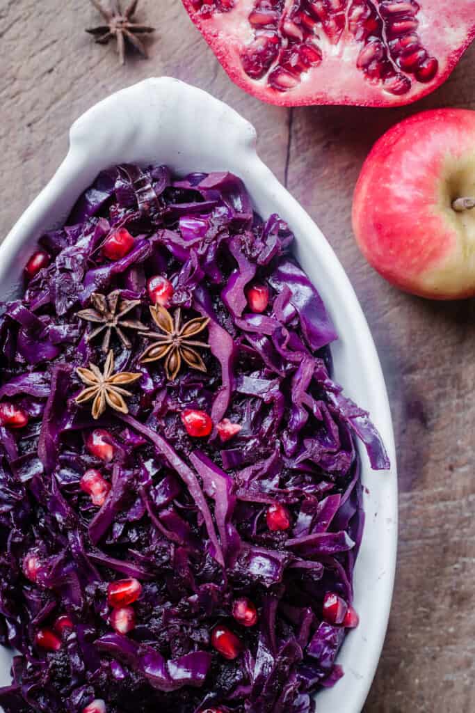 Braised Red Cabbage sprinkled with pomegranate seeds and star anise in a white dish on a wooden board