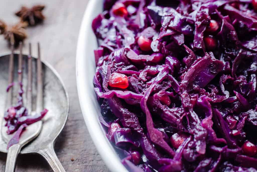 Close up of Braised Red Cabbage sprinkled with pomegranate seeds and star anise in a white dish on a wooden board