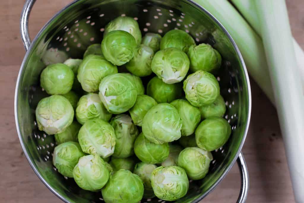 brussel sprouts in a colander next to leeks