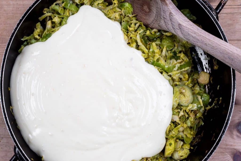 Cheese sauce being poured over brussel sprouts and leeks