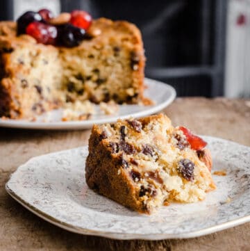 A slice of Gluten-Free Fruit Cake on a plate in front of the rest of the cake
