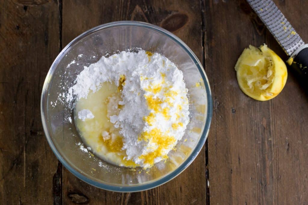 Glass mixing bowl filled with lemon icing ingredients