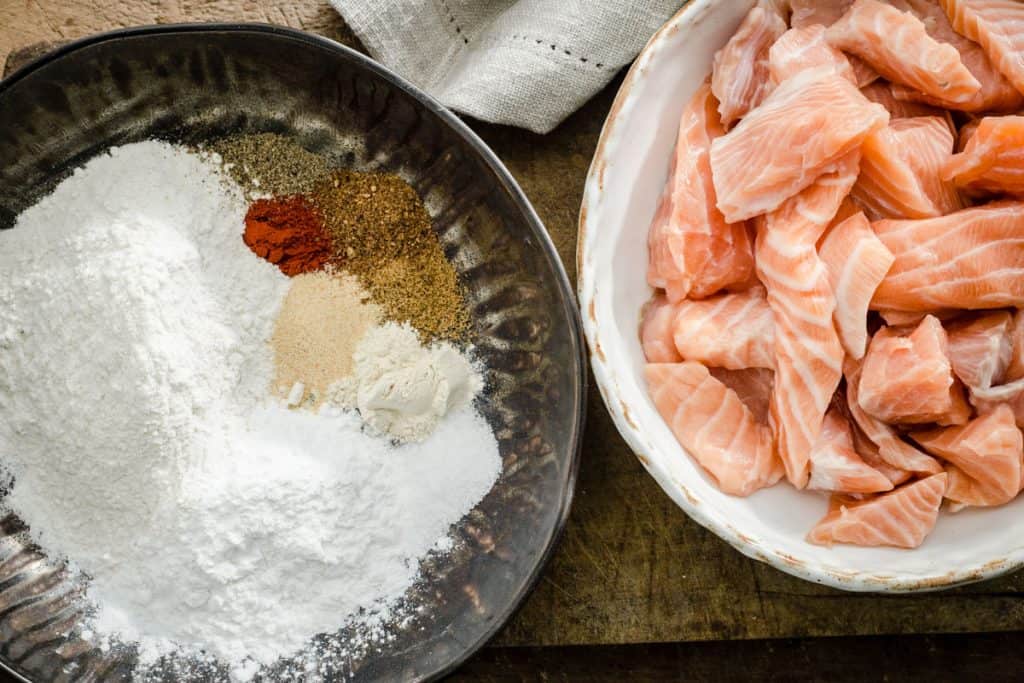 Two bowls, one with salmon pieces, on with flour and seasonings