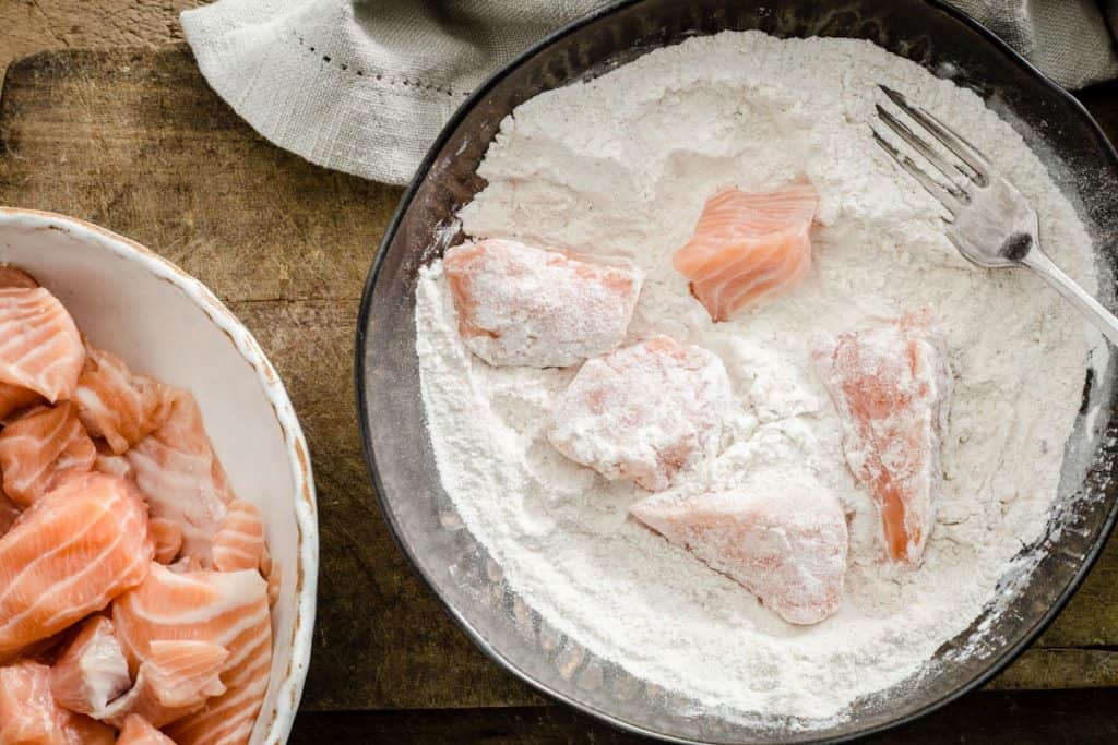 pieces of salmon being dipped into a flour coating in a bowl