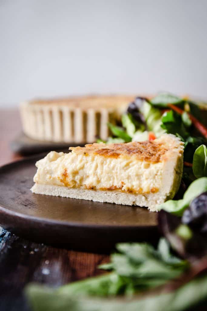 A slice of gluten-free quiche on a wooden plate surrounded by salad