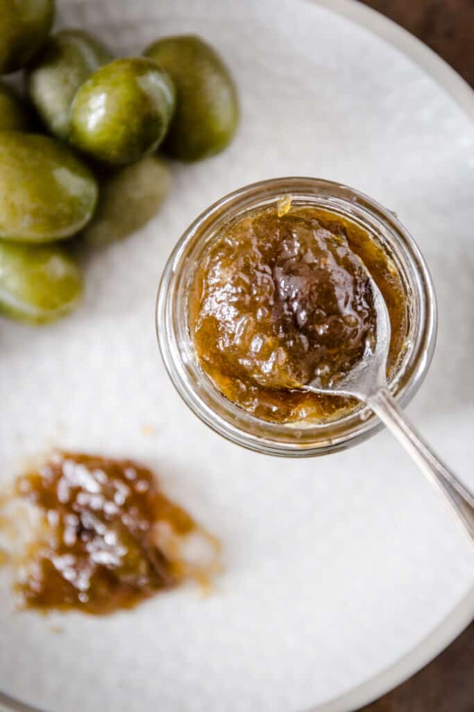 Green plum jam on a spoon on a plate with a jar of jam and green plums