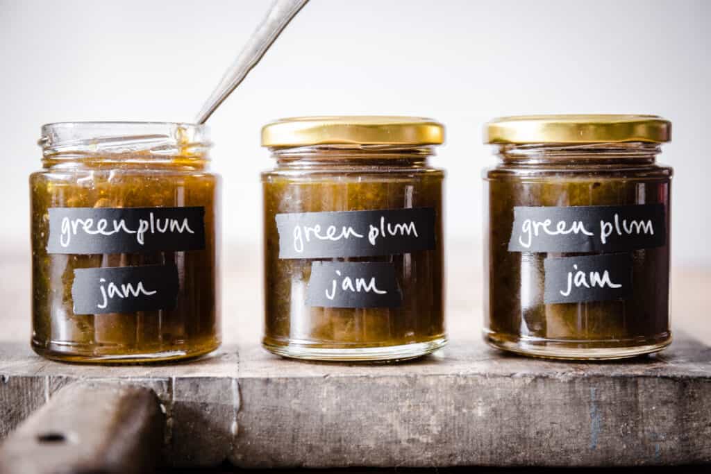 3 jars of green plum jam on wooden board