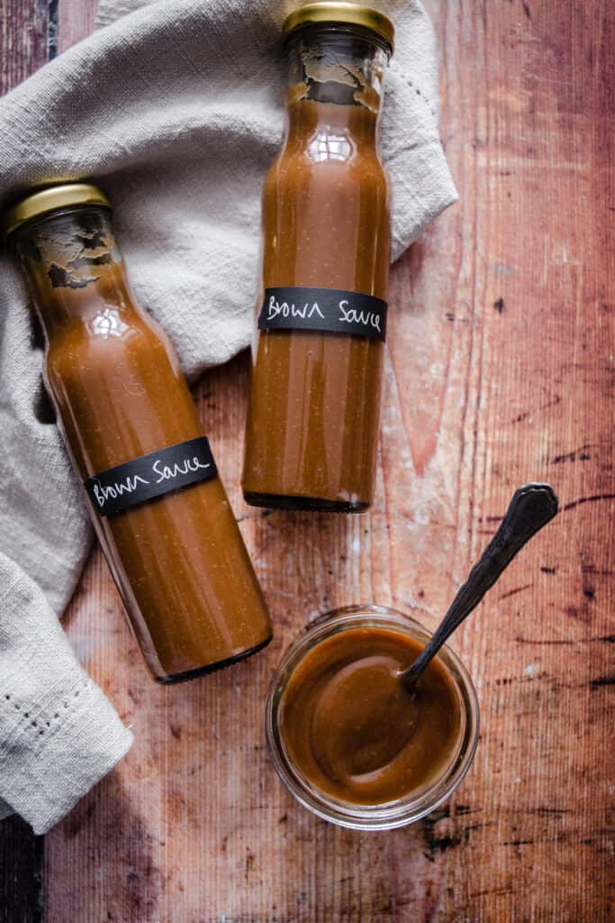 bottles of brown sauce on a table next to a pot of it