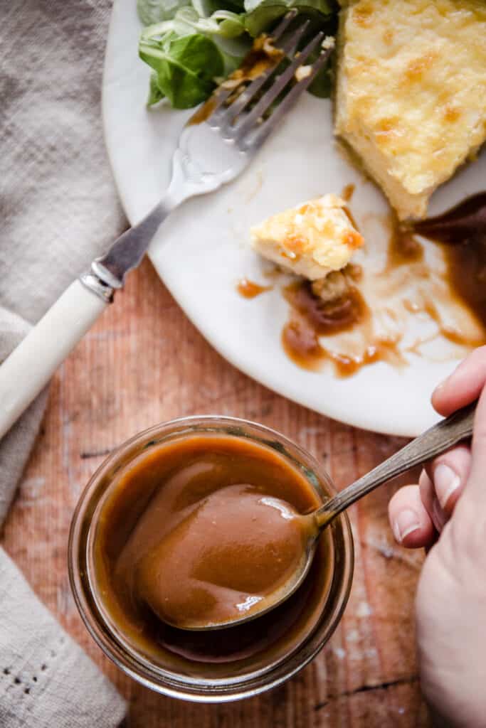 hand reaching into a pot of brown sauce, next to a plate of quiche and brown sauce