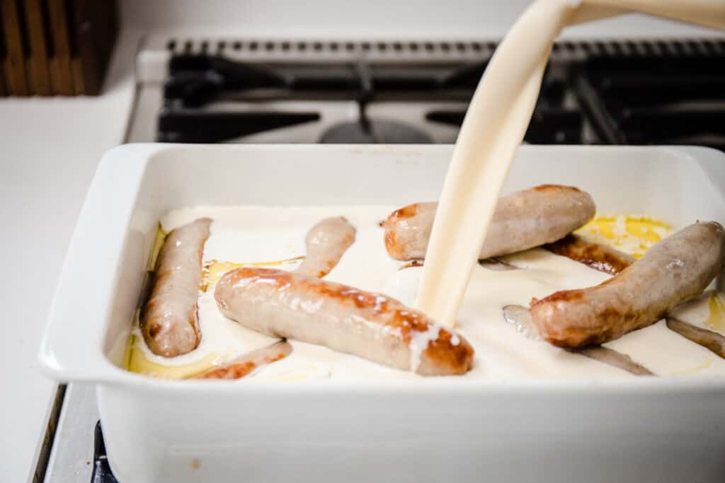 Batter being poured into a roasting dish full of sausages