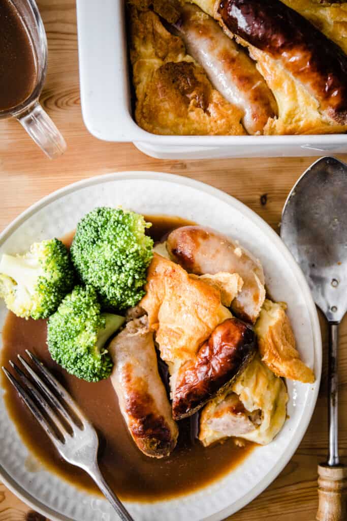 a portion of Toad in the Hole on a plate with broccoli and gravy