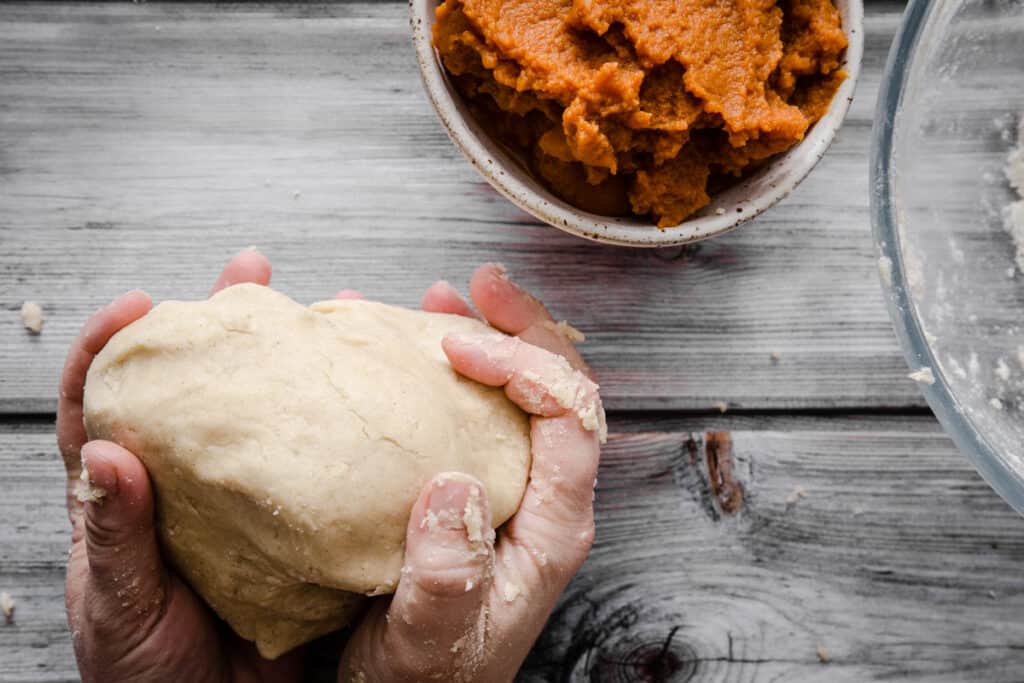 hands holding gluten-free pastry dough infront of a bowl of pumpkin