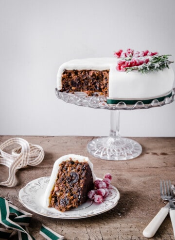 Slice of Christmas Cake on a plate in front of whole cake on a stand