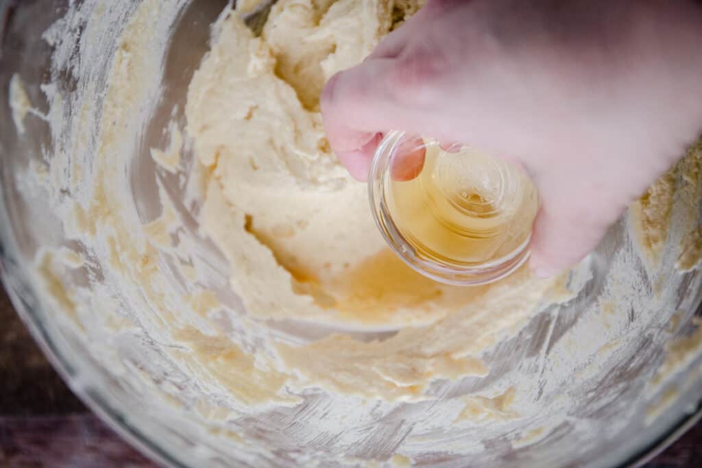 Hand pouring rum into frangipane batter in a glass mixing bowl