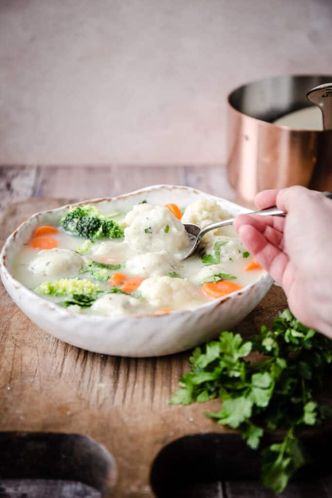 pale dumplings floating in a stew with carrot and broccoli