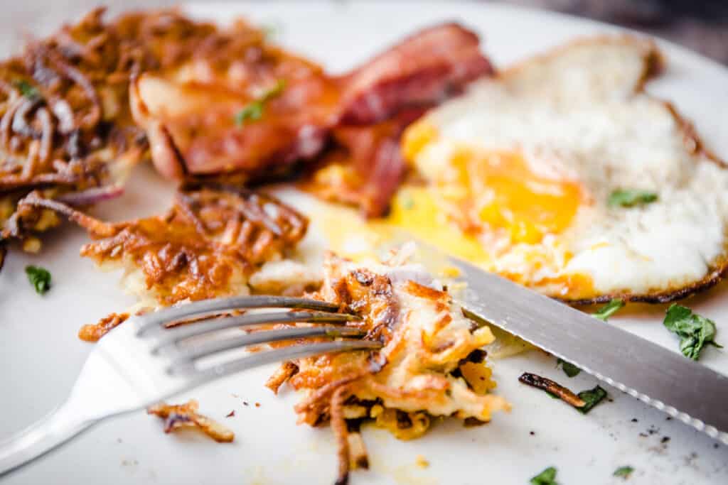 A fork taking a piece of hash browns on a plate of breakfast food