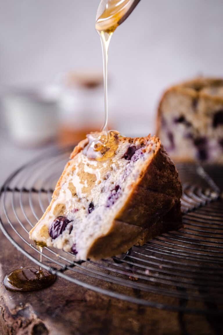 honey being drizzled over a slice of Porridge Cake on a wire rack