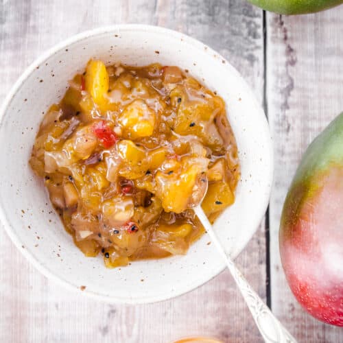 overhead image of mango chutney in a white bowl next to mangoes and stem ginger