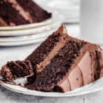 slice of chocolate cake on a plate with fork ful removed showing moist and tender sponge and creamy frosting.
